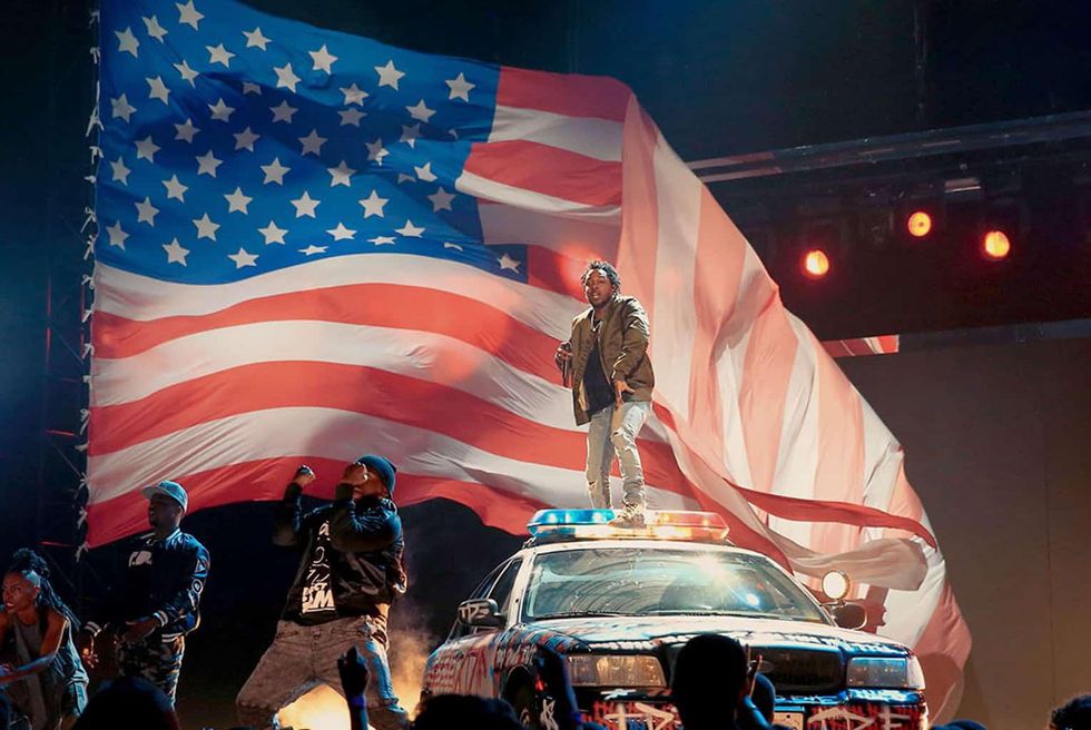 Kendrick Lamar performing on a cop car in front of an American flag